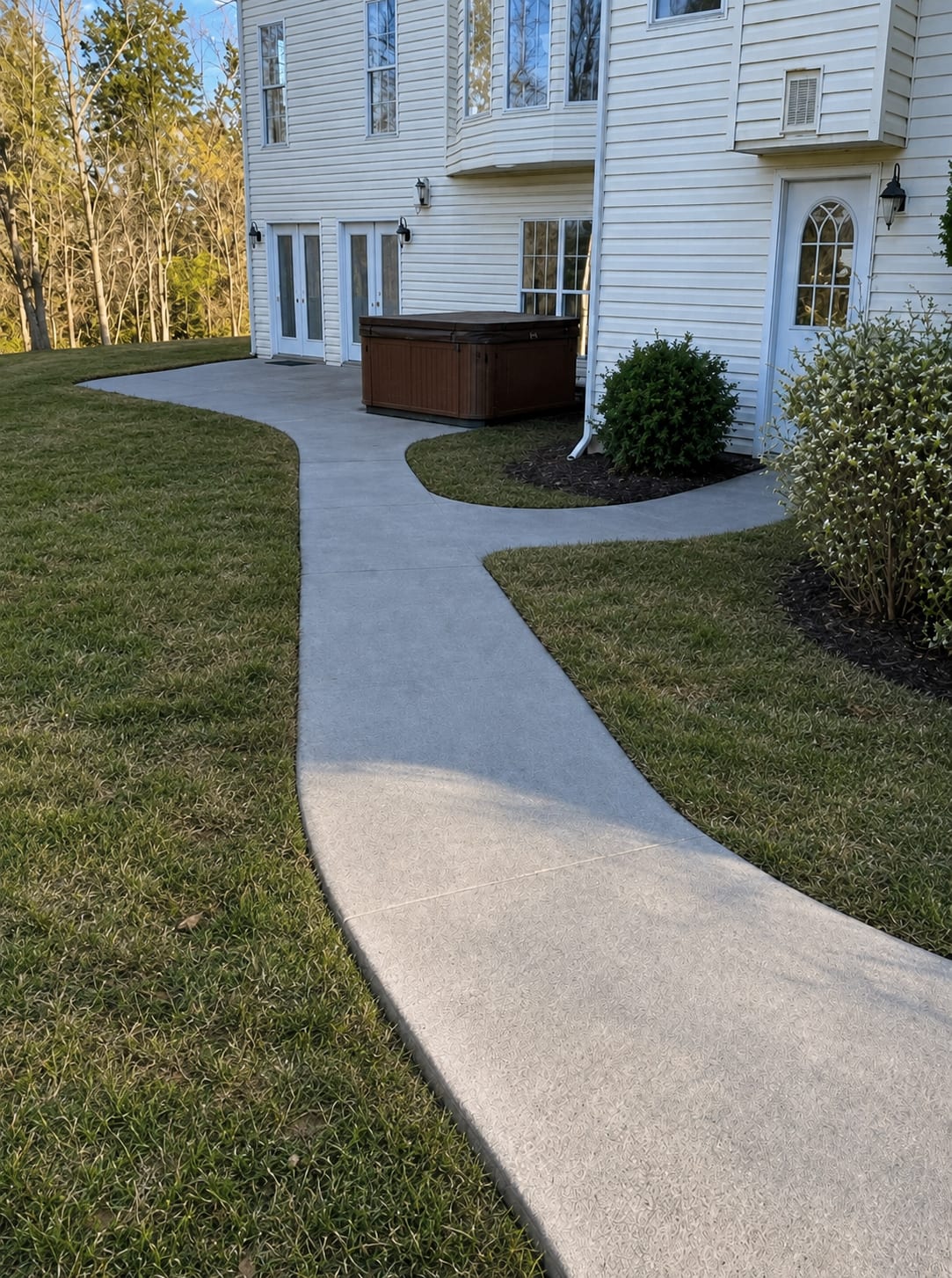 Curved stamped concrete walkway winding through a lawn to a patio and hot tub